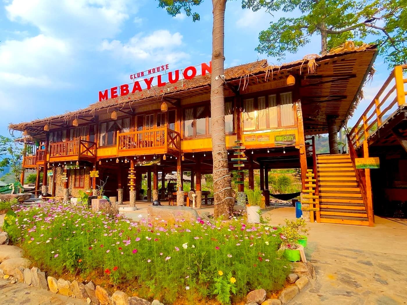 Mebayluon Clubhouse at the landing field: a two-storey wooden stilt house with a thatched roof and red sign