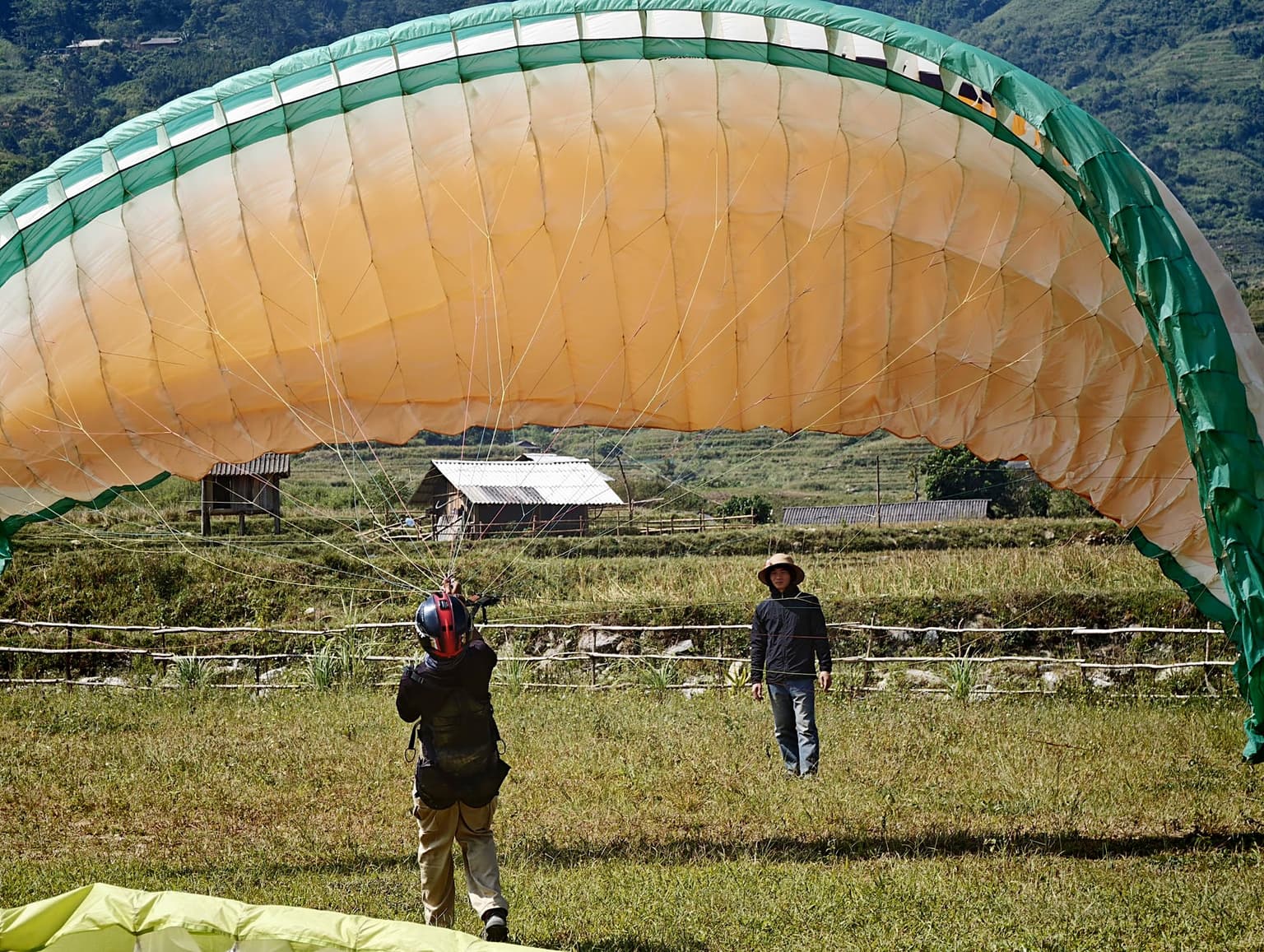 A student inflating before the launch run; the instructor stands close, watching wing and pilot.