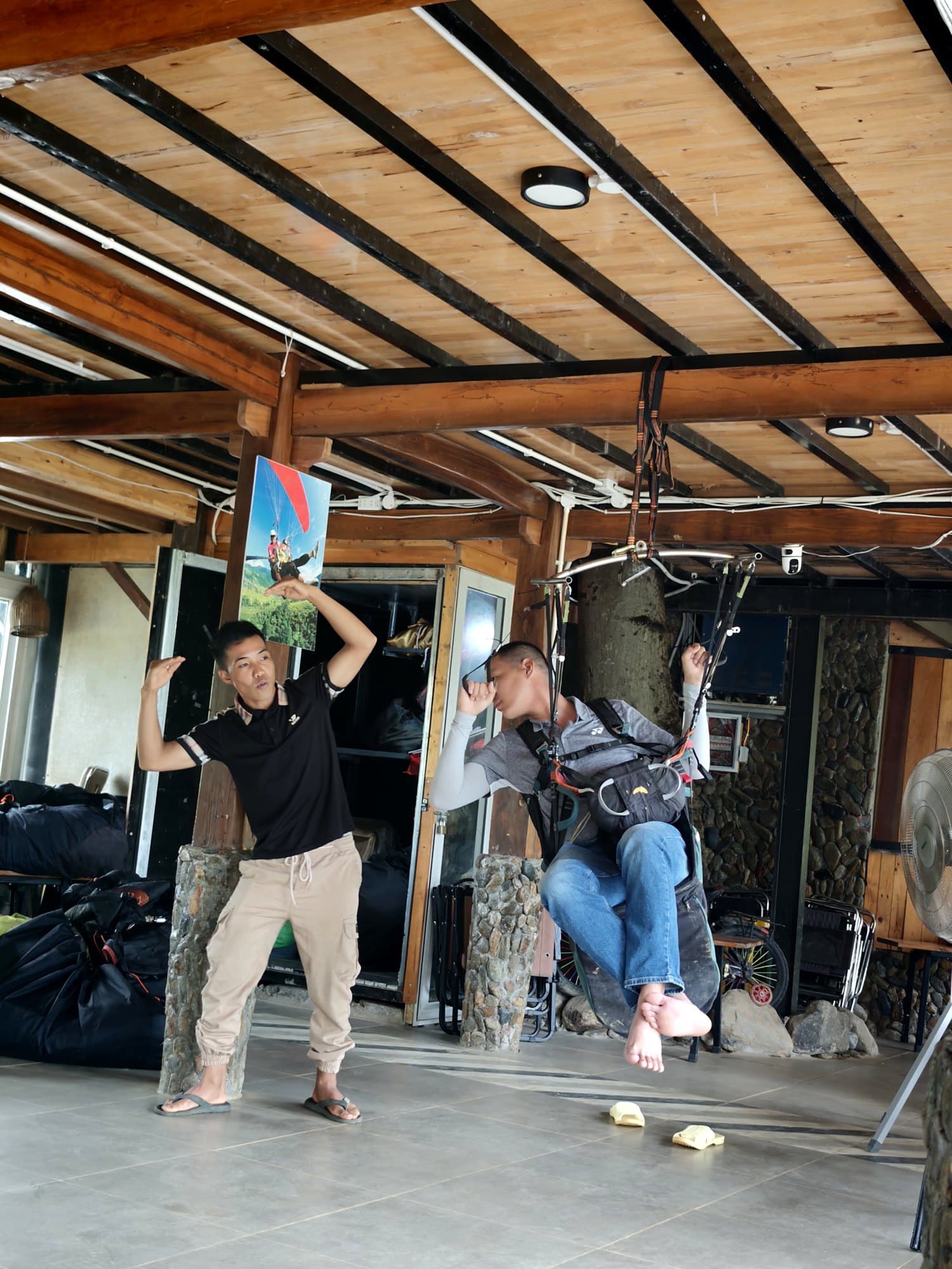 The simulator under the Clubhouse veranda: hanging in the harness, the student copies the instructor, both hands up as in straight flight.