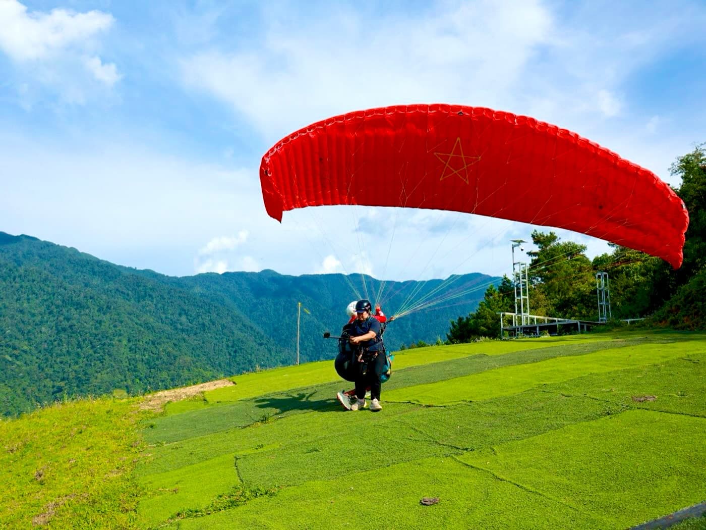 A tandem pair running down the Khau Pha turf launch under a fully inflated red flag wing